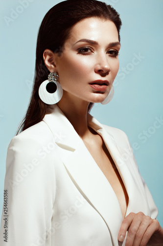 Beautiful girl with classic make-up and hair-style in a trendy designer white jacket posing in a studio. Beauty face.