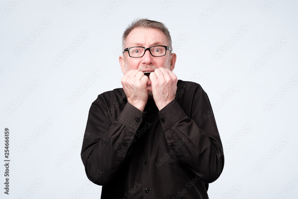 Nervous senior man in glasses bites nails, looks worried before visiting doctor Nervous senior man in glasses bites nails, looks worried before visiting doctor