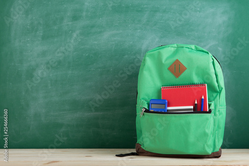 green backpack, calculator and notebook on the background of the blackboard