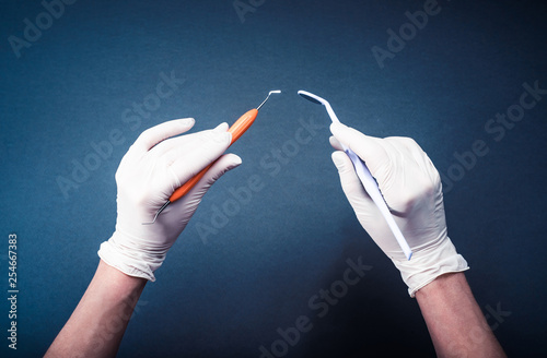 Hands in white gloves holding dental tools on dark blue background photo