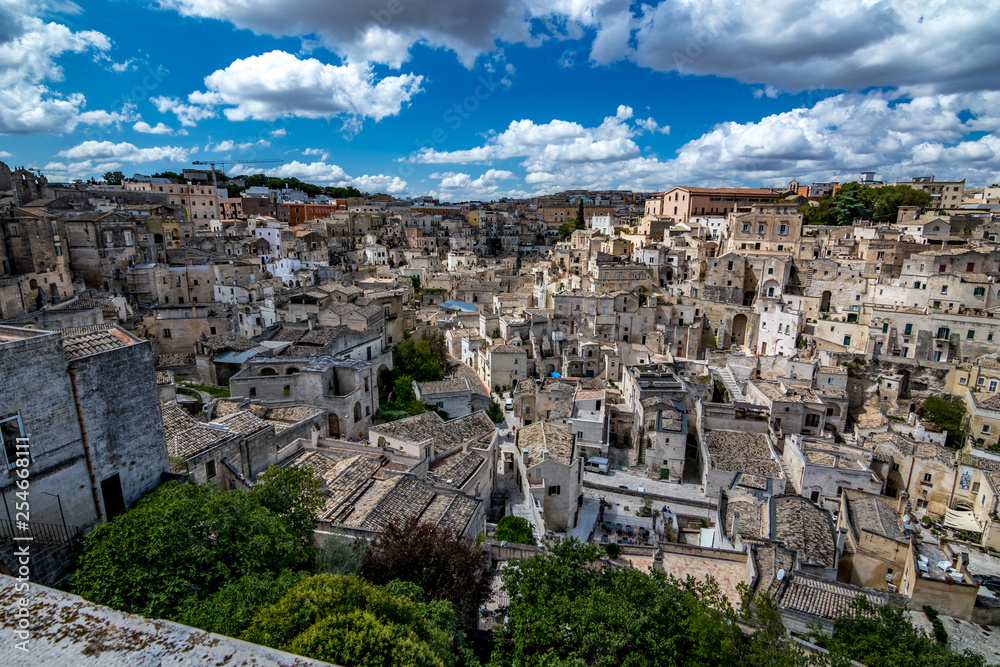 Summer day scenery street view of the amazing ancient town of the Sassi with white puffy clouds moving on the Italian blue sky. Matera, Basilicata, Italy
