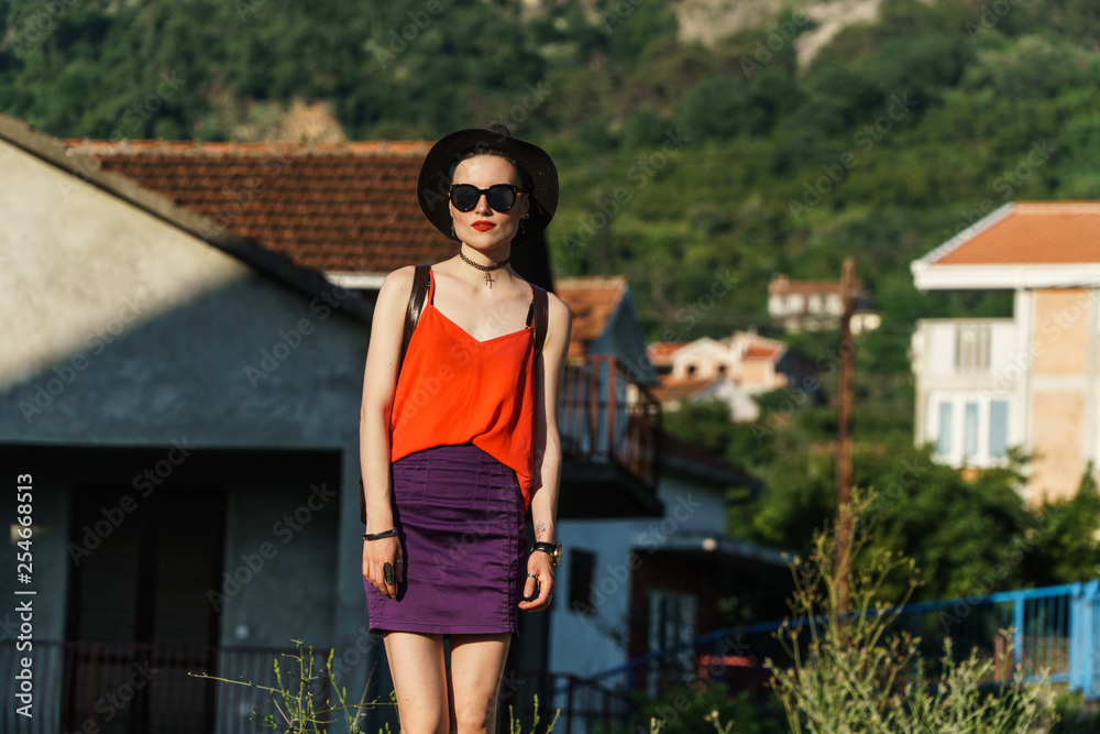 Girl in the summer in a black hat and sunglasses stands on the street