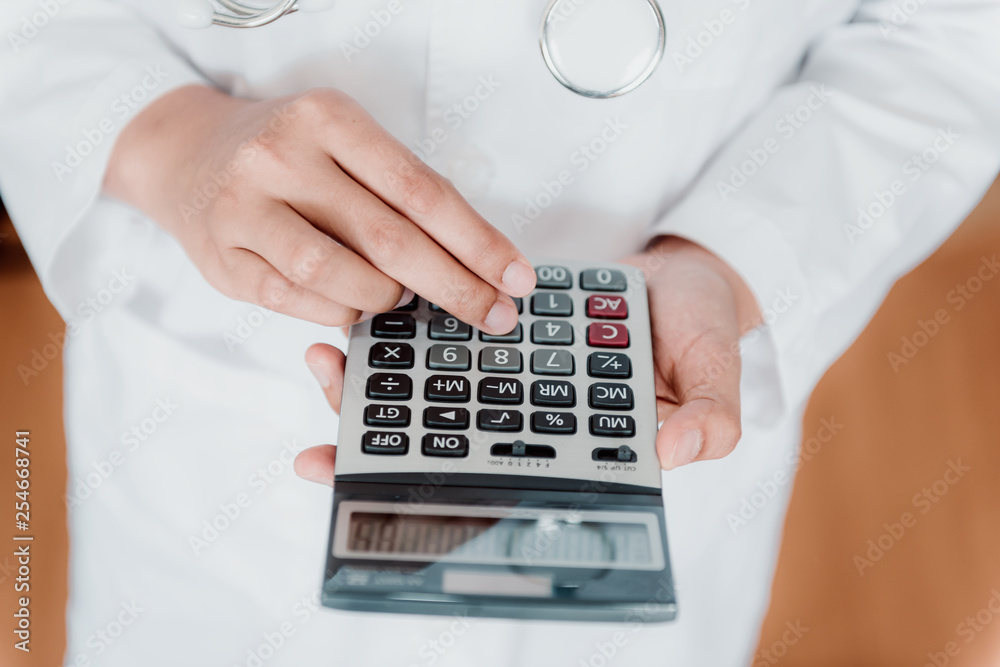 Close-Up of Female Doctor is Calculating Medicine Cost in Office Hospital, Female Medical is Using Calculator. Healthcare and Financial Concept. Close-Up of Female Doctor is Calculating Medicine Cost in Office Hospital, Female Medical is Using Calculator. Healthcare and Financial Concept.