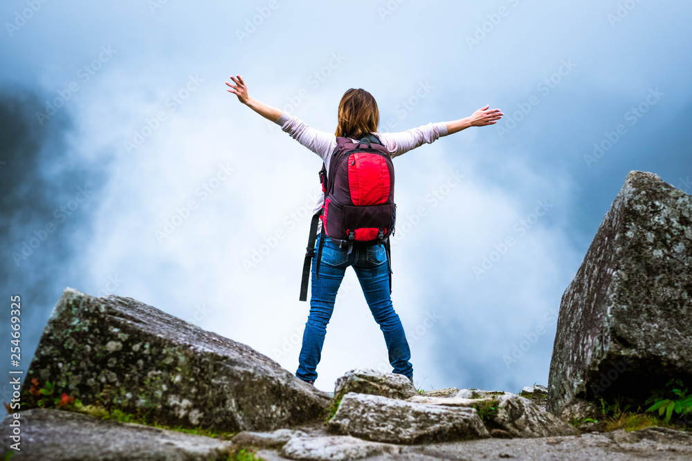 Girl with backpack in misty mountains with hands up