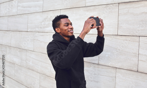 фотографія Cheerful smiling african man taking selfie picture by phone on city street over