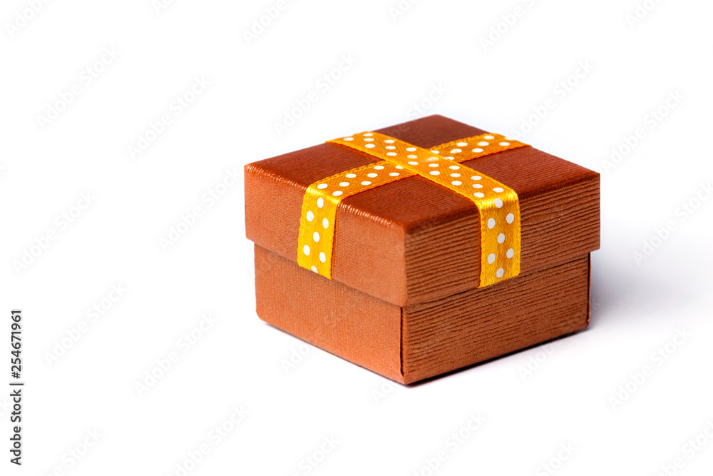A small closed classic golden surprise gift box with a ribbon, present for any occasion. Engagement ring box concept isolated on white background. A small closed classic golden surprise gift box with a ribbon, present for any occasion. Engagement ring box concept isolated on white background.
