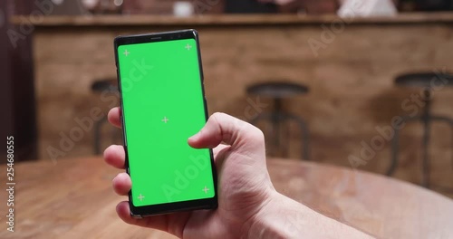 Swiping on a phone with green screen in a vintage cafe. Man holds a modern smartphone