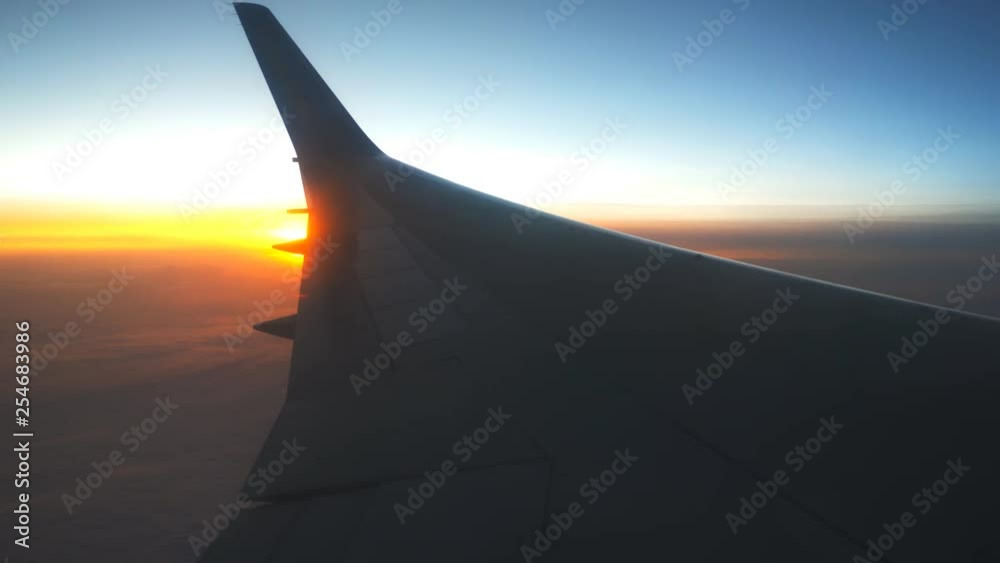 View from airplane window to sunrise or sunset. Wing of plane flying above the clouds with sun light. Aircraft flight at sky. Concept of traveling by air. Trip by airliner with beautiful background View from airplane window to sunrise or sunset. Wing of plane flying above the clouds with sun light. Aircraft flight at sky. Concept of traveling by air. Trip by airliner with beautiful background