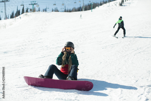Girl with a snowboard sitting on a snowy slope.