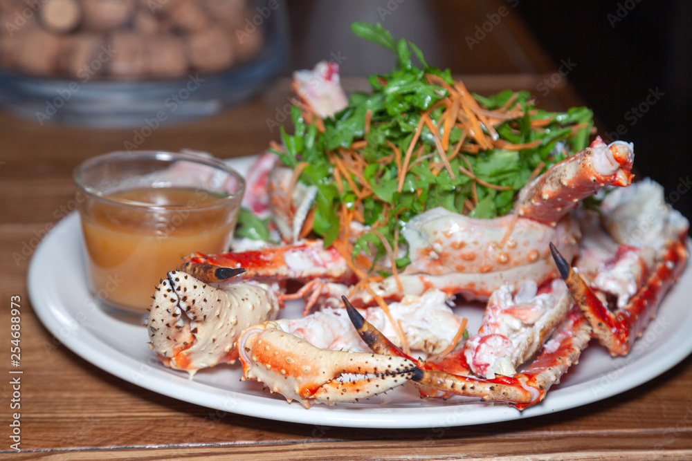 Closeup round white dish with fresh red big boiled prepared blue kamchatka crab with green, sauce. Concept useful seafood in a menu premium restaurant preparing, serving for guests, clients