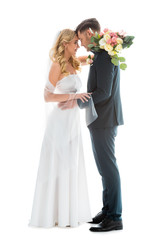beautiful bride in white wedding dress, and groom in elegant black suit standing face to face isolated on white