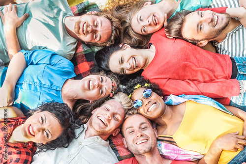 Group of diverse friends having fun outdoor - Happy young people lying on grass after picnic and laughing together - Friendship, unity, millennial and youth lifestyle concept