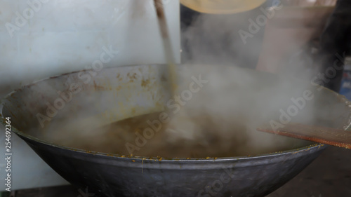 A man stir a dish of food in steam and smoke