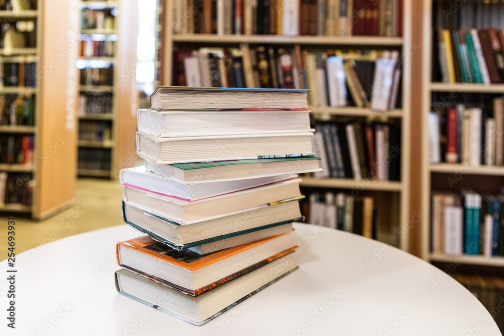 Book Stack On White Desk And Blurred Bookshelf On Background In The Library Room, Education Concept Book Stack On White Desk And Blurred Bookshelf On Background In The Library Room, Education Concept