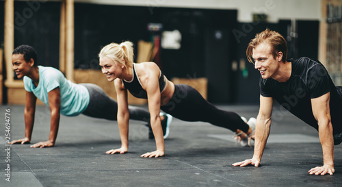 Smiling people doing pushups on a gym floor