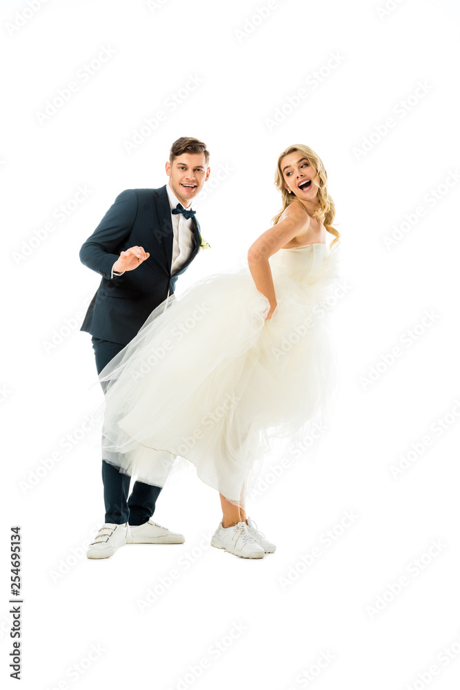 cheerful groom and bride dancing in elegant clothes and sneakers isolated on white