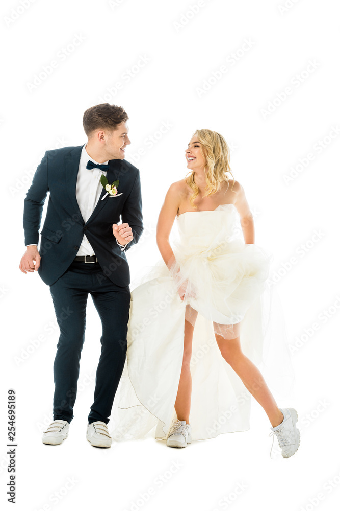 happy groom and bride dancing in elegant clothes and sneakers while looking at each other isolated on white happy groom and bride dancing in elegant clothes and sneakers while looking at each other isolated on white