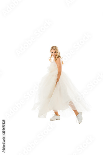 beautiful groom in wedding dress and sneakers dancing while looking at camera isolated on white