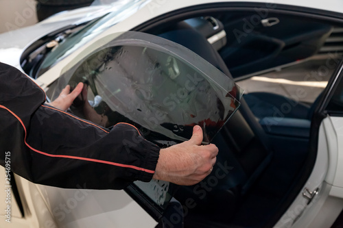 The wizard for installing additional equipment sticks a tint film on the side front glass of the car and flattens it by hand to fit the glass with a greenish tint in the auto service.