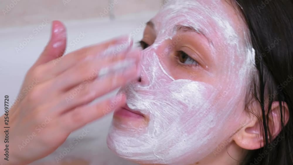 Beautiful brunette woman puts a mask on the face lying in the bathroom at home. Face close-up. Beautiful brunette woman puts a mask on the face lying in the bathroom at home. Face close-up.