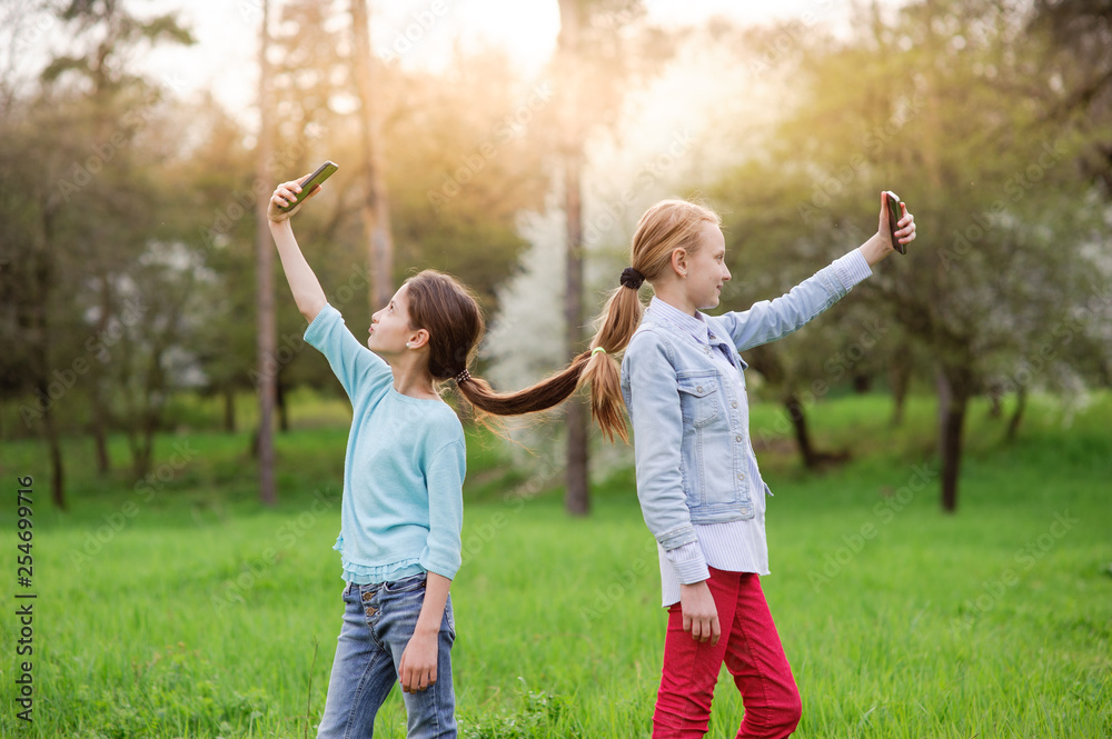 Fototapeta premium two funny little girls with connected hair taking selfie photo using cell phone in spring green park outdoor leisure
