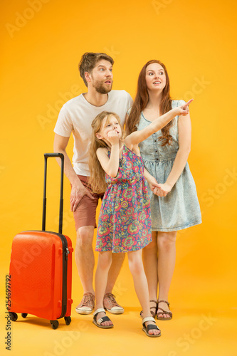 Happy surprised parent with daughter and suitcase at studio isolated on yellow background. Travel, vacation, parenthood, togetherness, tourism concept.