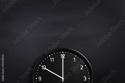 Black wall clock on black chalkboard background. Crop composition with your copy