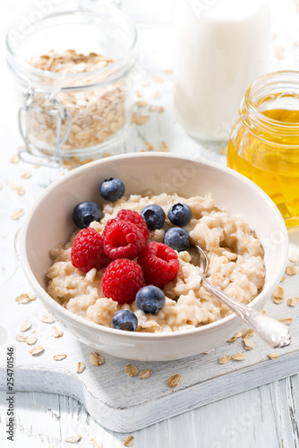 homemade oatmeal with berries for breakfast on white wooden board, vertical closeup