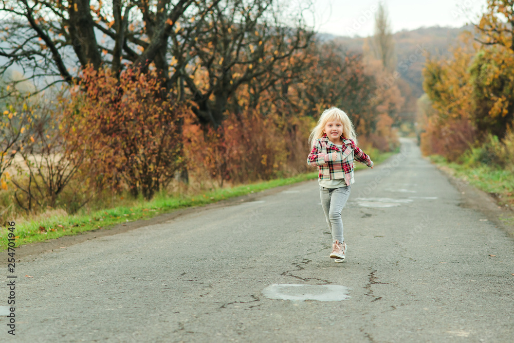 Little girl running down the road in autumn time. Happy child girl with long hair outdoors. Autumn holidays. Happy childhood. Autumn season. Walking on nature. Little girl running down the road in autumn time. Happy child girl with long hair outdoors. Autumn holidays. Happy childhood. Autumn season. Walking on nature.