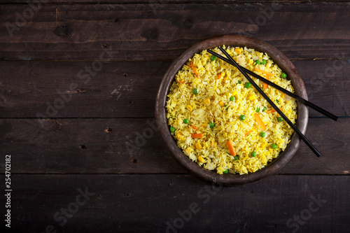 Cooked rice with curry and vegetables in a pan with chopsticks on the wood black background.
