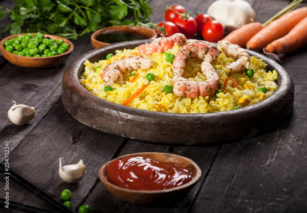 Cooked rice with shrimps, curry and vegetables in a dish on the wood black bamboo background. Cooked rice with shrimps, curry and vegetables in a dish on the wood black bamboo background.
