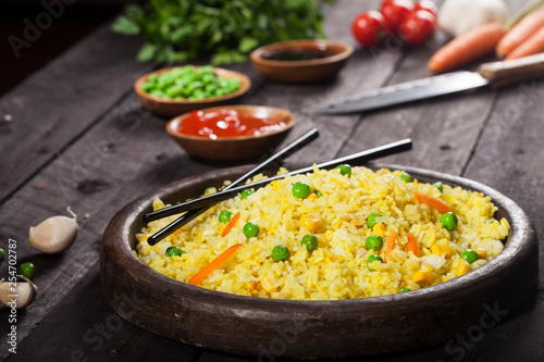Cooked rice with curry and vegetables in a pan with chopsticks on the wood black background.