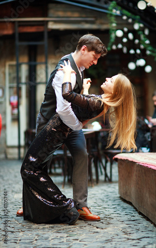 Joyful young couple in love dancing latin on evening street near the cafe of old town