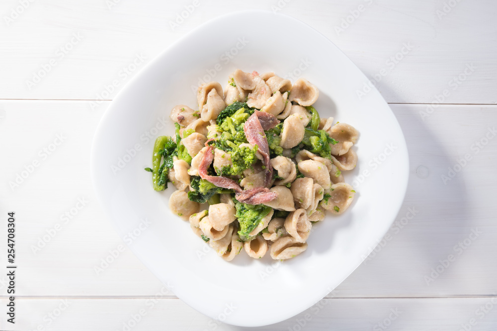 Classical dish of Apulia region pasta Orecchiette with turnip greens and salted anchovies, top view, white wooden background