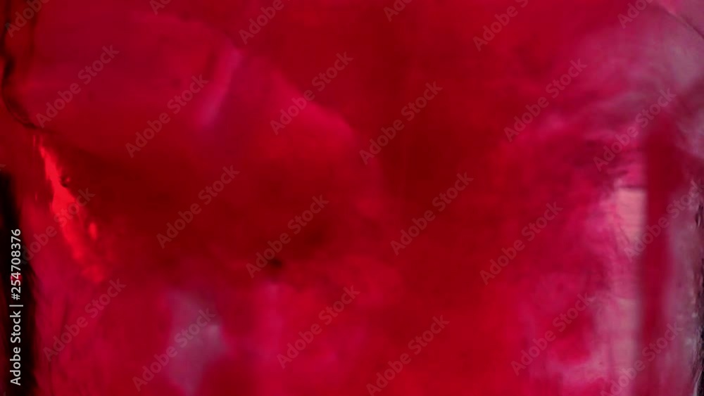 close up view of red liquid pouring into glass with ice cubes and water close up view of red liquid pouring into glass with ice cubes and water