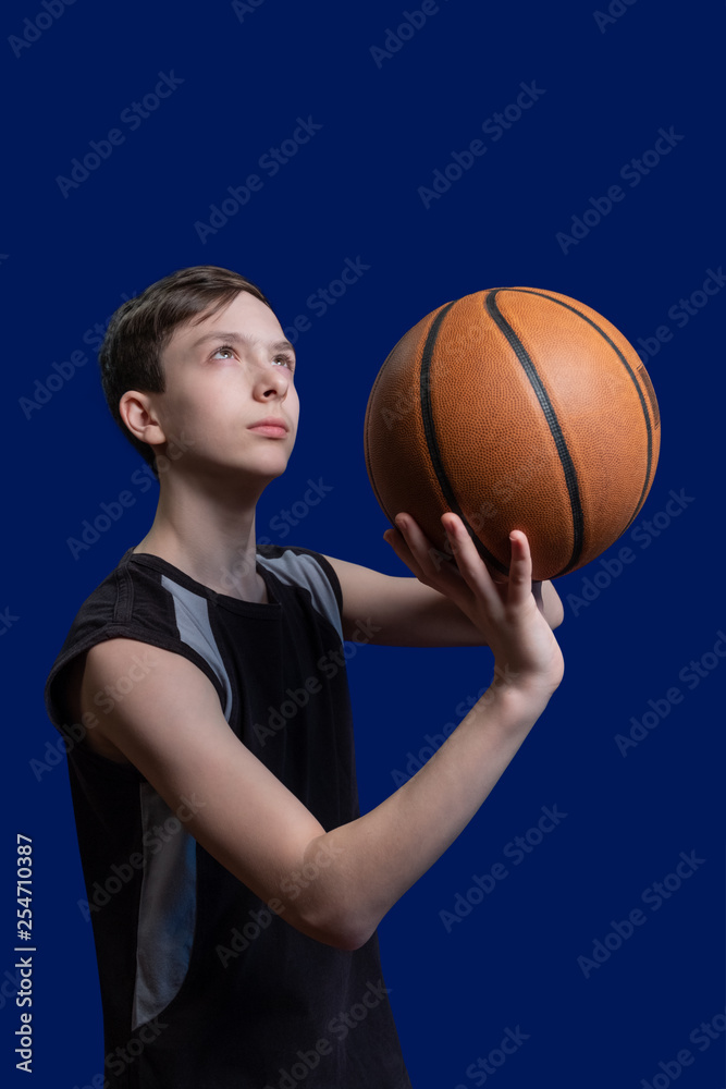 Basketball. The guy in the black T-shirt is preparing to throw the ball. Blue background. Teen basketball player.