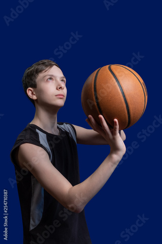 Basketball. The guy in the black T-shirt is preparing to throw the ball. Blue background. Teen basketball player.