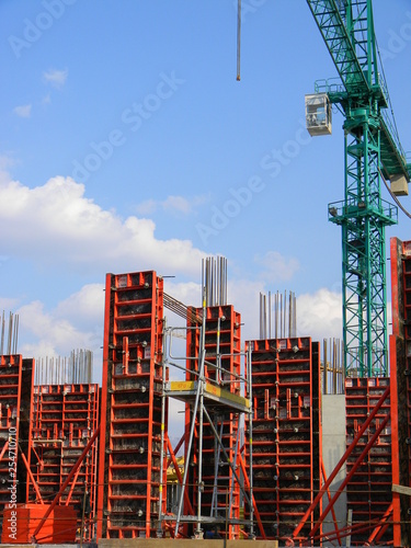 A green construction crane hovering above reinforced concrete columns at a construction site, Tirana, Albania