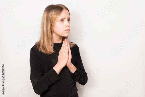 Young teenage girl praying on a light background. The girl has a sad face