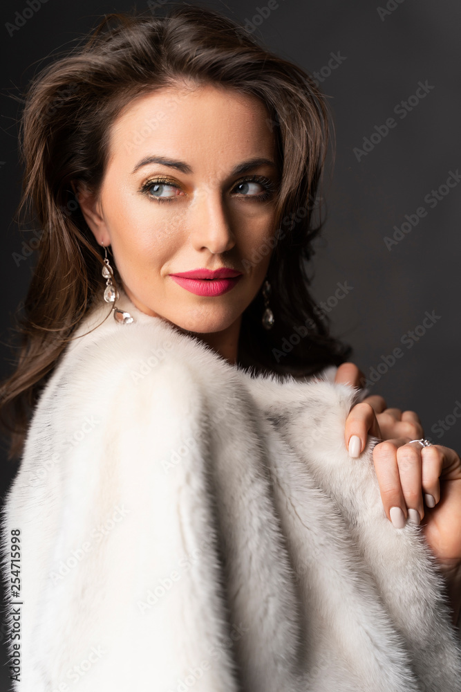 Close up portrait of a elegant beautiful brunette woman dressed in a fur coat thrown over her shoulders on a gray background. Advertising and commercial design. Copy space Close up portrait of a elegant beautiful brunette woman dressed in a fur coat thrown over her shoulders on a gray background. Advertising and commercial design. Copy space