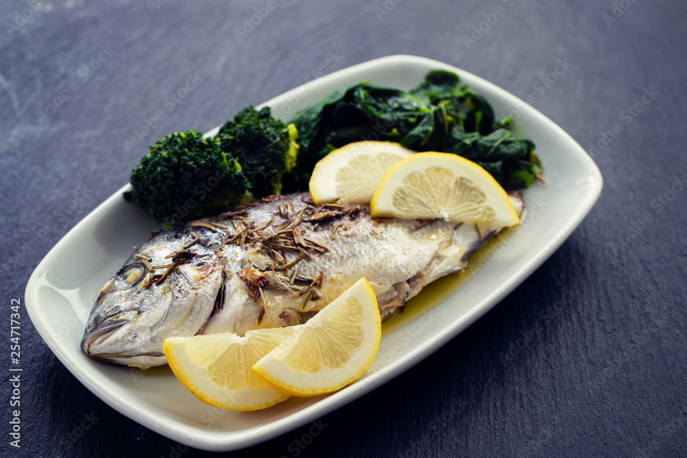 baked fish with lemon in white dish on ceramic background baked fish with lemon in white dish on ceramic background