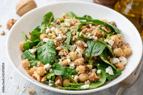 Healthy salad with spinach, chickpeas, quinoa, feta cheese and walnuts in white plate on concrete background. Selective focus.