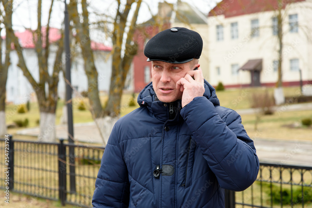 The man in the jacket and cap speaks on the phone. The man in the jacket and cap speaks on the phone.