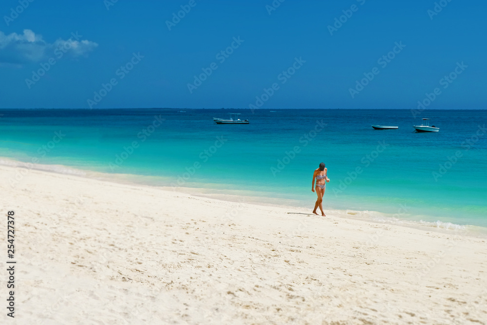 Slender girl walking on a white sandy beach in search of shells