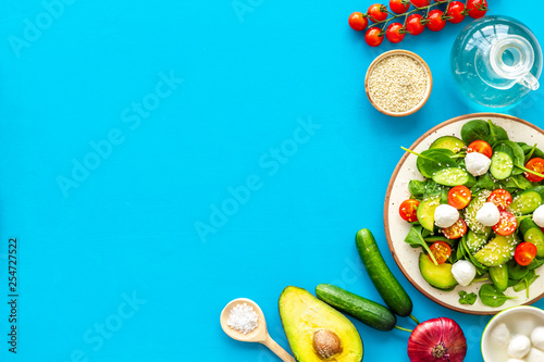 Cooking fresh salad. Vegetables, greens, spices, plate of salad on blue kitchen desk top view space for text