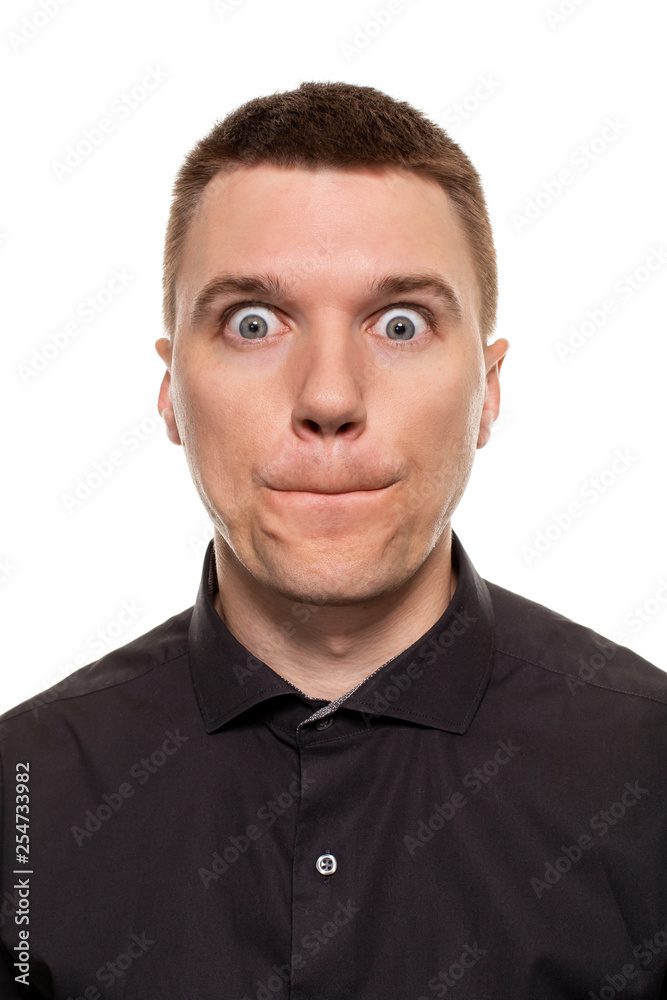 Handsome young man in a black shirt is making faces, while standing isolated on a white background