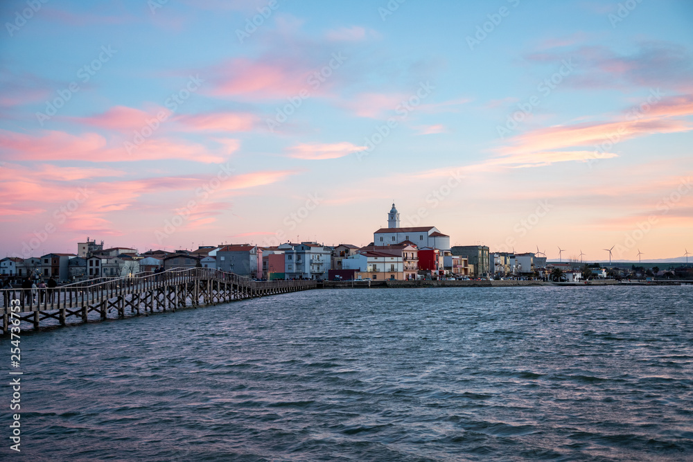Fototapeta premium the panorama of Lesina and jatty on lake (lagoon) at sunset. Gargano National Park, Apulia, Italy