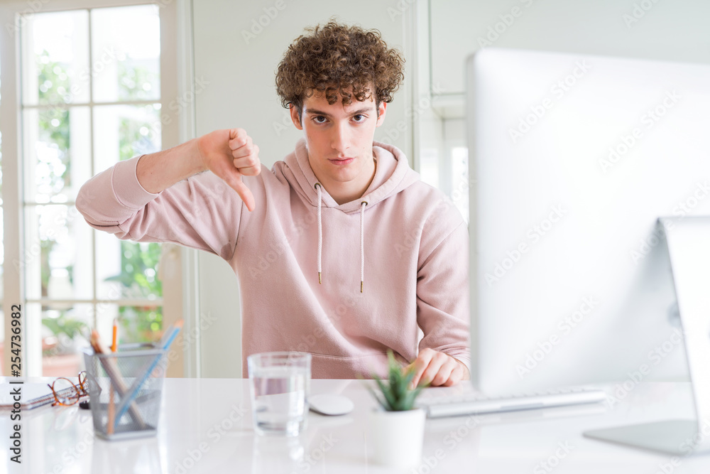 Young student man using computer with angry face, negative sign showing dislike with thumbs down, rejection concept Young student man using computer with angry face, negative sign showing dislike with thumbs down, rejection concept
