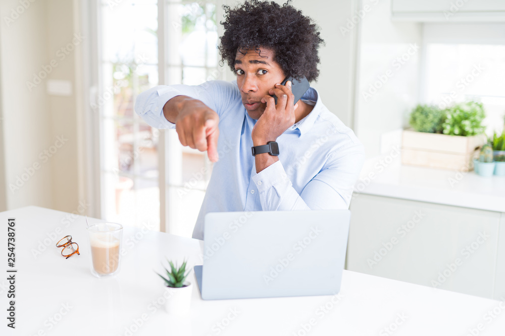 African American business man talking on the phone pointing with finger to the camera and to you, hand sign, positive and confident gesture from the front
