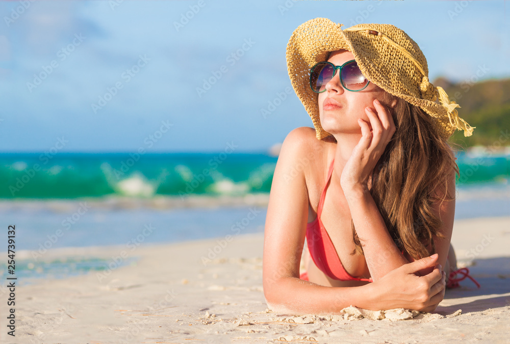 long haired woman in bikini and straw hat lying on tropical beach